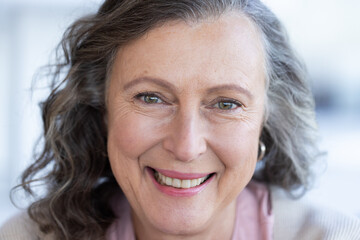 Smiling senior woman with grey hair looking at camera, close-up portrait