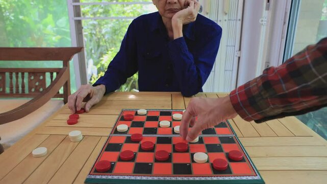 Senior asian father and son are enjoy playing checkers board game at home for leisure activities hobby and preventing from alzheimer symptom illness