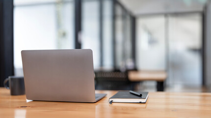 Rear view of simple workspace with laptop, notebooks, coffee cup and tree pot on white table with blurred office room background