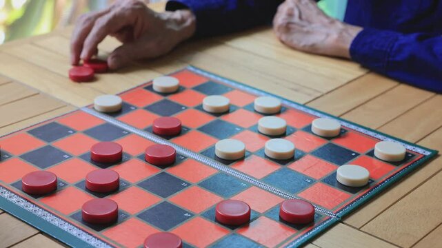 Senior asian father and son are enjoy playing checkers board game at home for leisure activities hobby and preventing from alzheimer symptom illness