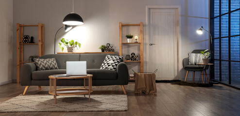 Interior of living room with comfortable sofa, table, racks and glowing lamps