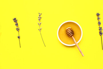 Bowl of sweet lavender honey, dipper and flowers on yellow background