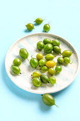 Plate with fresh gooseberries on blue background