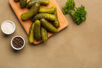 Wooden board with pickled cucumbers and different spices on brown background