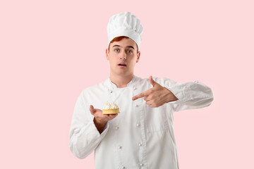 Shocked male confectioner in uniform pointing at lemon tartlet on pink background