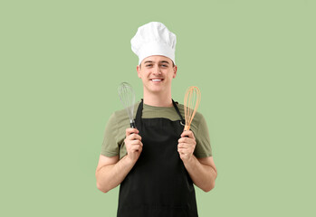 Male confectioner in apron with whisks on green background
