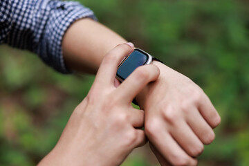 Close up, man using smart watch, setting up his smart watch in the forest, goal achievement, sport and fitness concept outdoors in nature..