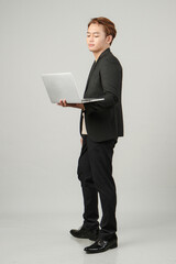 full lenght shoot of pensive asian business man wearing suit holding laptop computer on isolated background