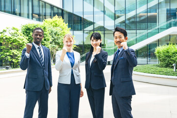 オフィスビルの前でガッツポーズする多国籍ビジネスパーソンのグループ