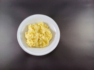 Smooth and creamy mashed potato served in a white bowl, set against a dark grey ash background, offering a comforting and visually striking contrast between the light dish and the moody backdrop