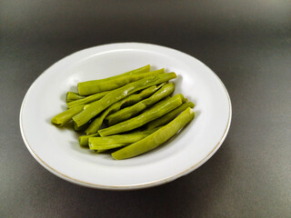 Chopped green beans neatly placed in a white bowl, set against a contrasting dark grey ash background, creating a visually striking and appetizing presentation