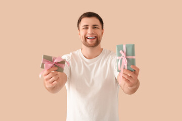 Handsome happy young man with gift boxes on beige background