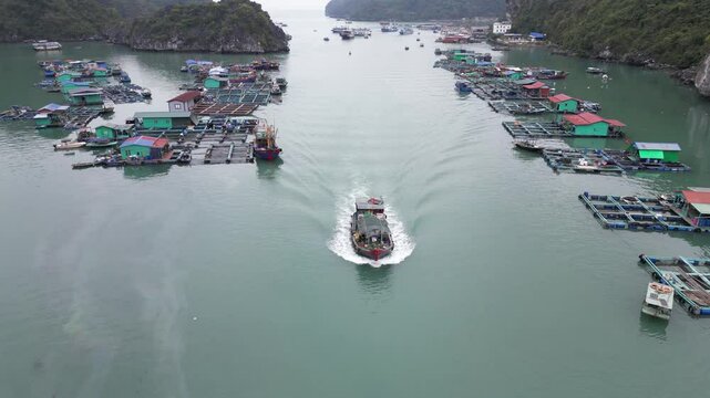 drone shot of fishing vessel going through floating village in Cat Ba and Halong Bay in Northern Vietnam