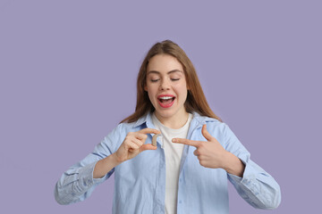 Happy young woman pointing at hearing aid on lilac background