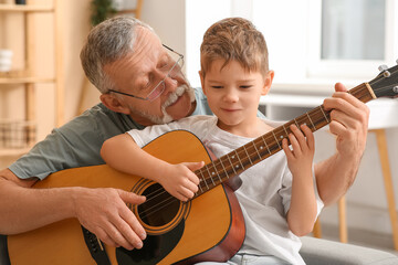 Grandfather teaching his cute little grandson playing guitar at home