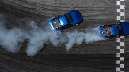 Aerial top view two cars drifting battle on asphalt race track with lots of smoke from burning tires, Two race cars competition drift battle view from above. © Kalyakan