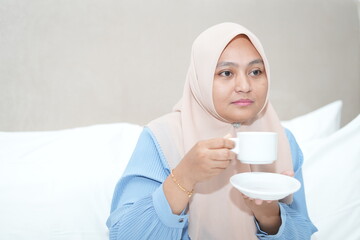 Muslim woman is relaxing while enjoying a cup of tea on the bed