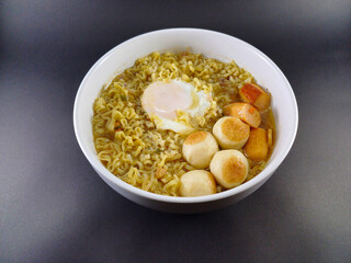 Indomie Rebus with Sausages, Meatballs, and Sunny Side Up Egg: Flavorful Indonesian Noodle Dish Served in a White Bowl, Perfectly Complemented by a Dark and Ash Abstract Background