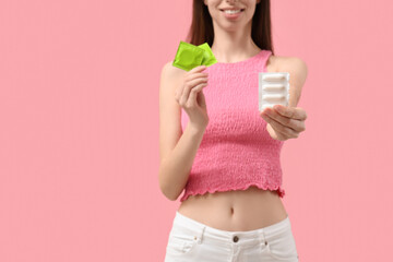 Young woman with condoms and vaginal suppositories on pink background