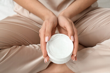 Woman in silk pajamas holding jar of cream, closeup