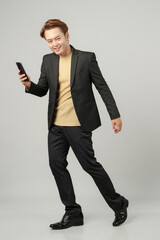 full length shoot of cheerful happy asian business man wearing suit holding mobile phone on isolated background.