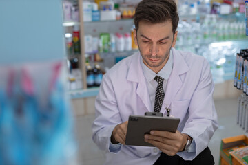 man pharmacists are selecting medications for patients online via tablet in drug store. Drug seller use tablet check for information before sending to patient.