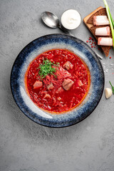 Tomato Soup with beef cabbage and vegetables in a blue plate on a gray background. Russian soup Borscht with tomato paste and sour cream, top view and copy space