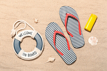 Flip flops with bottle of sunscreen, seashells and lifebuoy ring on sand