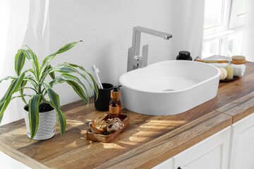 Fototapeta premium Chest of drawers with sink, houseplant and bath supplies near white wall in bathroom