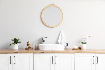 Modern sink, bath supplies on chest of drawers and mirror on light wall in bathroom