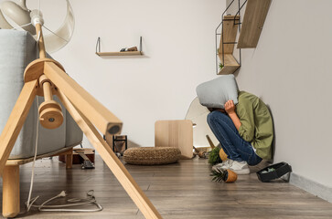 Young woman with pillow sitting near wall during earthquake at home