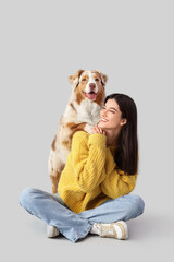 Young woman with Australian Shepherd dog sitting on light background © Pixel-Shot