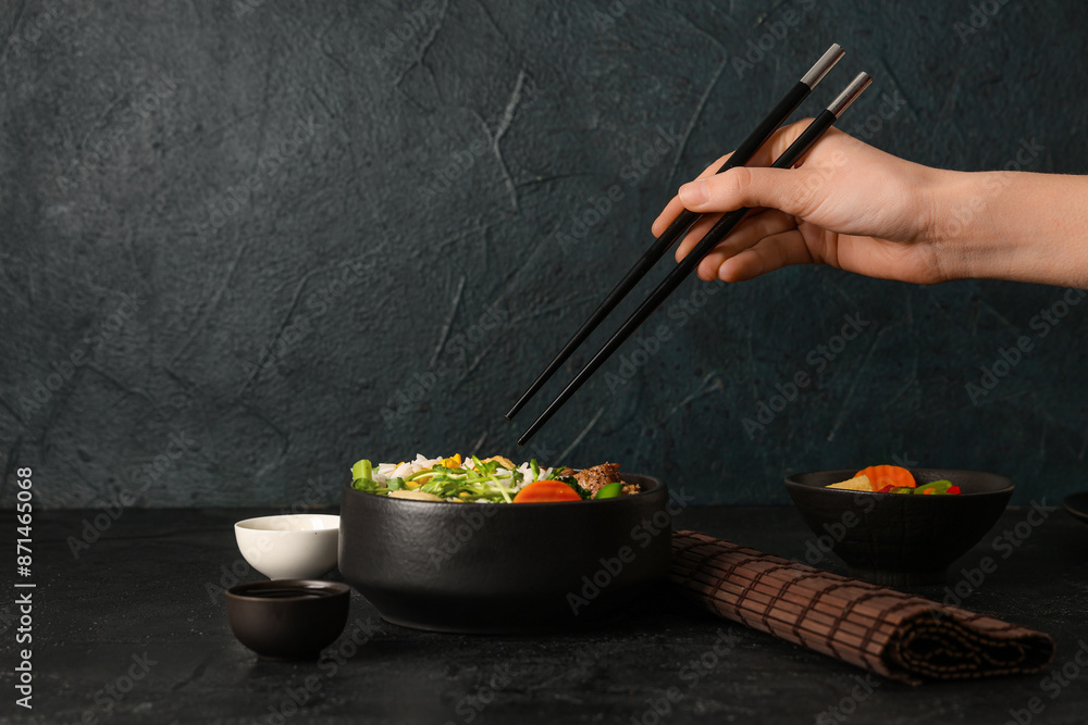 Sticker Female hand with chopsticks, bowl of tasty rice and soy sauce on dark table