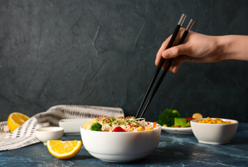 Woman eating tasty rice with chopsticks on table against dark background