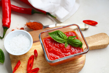 Glass bowl of tomato sauce with basil and chili peppers on white background