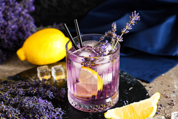 Glass of fresh lavender lemonade with flowers and lemons on grey table