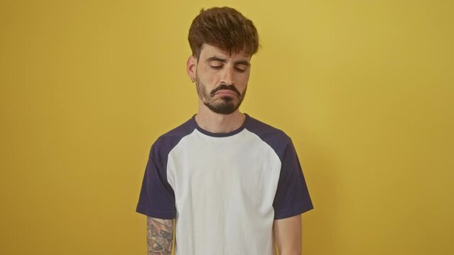 Young hispanic man, looking worryingly sad and depressed, standing alone over yellow background, crying out his stress and anger, disheartening isolation echoing in his expression