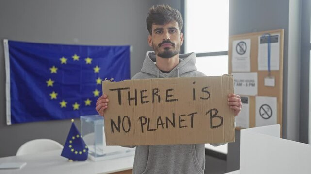 Handsome young hispanic man holding protest sign with european union flag indoors