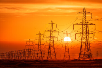 Sun setting behind the electric power lines running from Dungeness power station on the Kent coast south east England UK