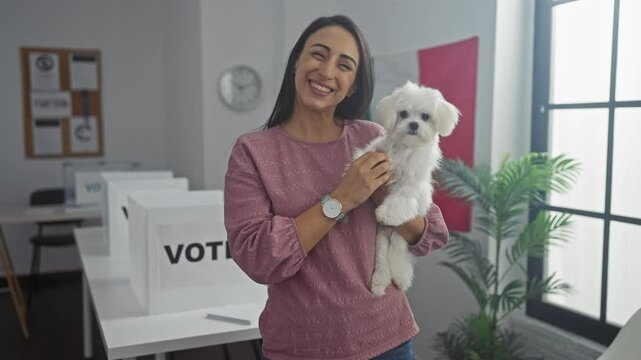 Hispanic woman holding a bichon maltes dog in an indoor college polling station with a banner.
