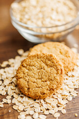 Tasty oatmeal cookies and rolled oat on wooden table.