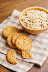 Tasty oatmeal cookies and rolled oat on checkered napkin on wooden table.