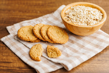 Tasty oatmeal cookies and rolled oat on checkered napkin on wooden table.
