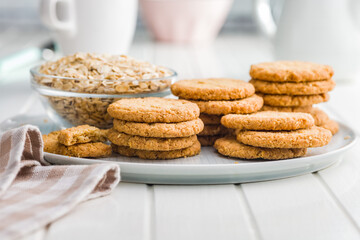 Tasty oatmeal cookies and rolled oat on plate on white table.