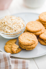 Tasty oatmeal cookies and rolled oat on plate on white table.
