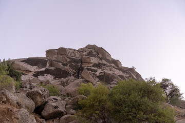 A rocky hillside with a few trees and a cloudy sky