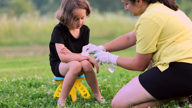 a mother applies spray to a child's hand after an insect, mosquito or bee bite in the summer in the yard