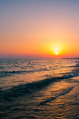 Sunset on the Mediterranean Sea. Natural seascape with calm waves and bright low sun. Side view of the water and beach. The concept of an evening walk. Coastline. Holidays in Italy. Nature wallpaper