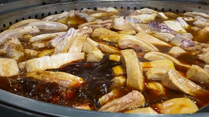 Pork ribs are being cooked on an industrial scale in large pans, simmering in a rich broth.