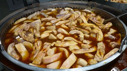 Pork ribs are being cooked on an industrial scale in large pans, simmering in a rich broth.